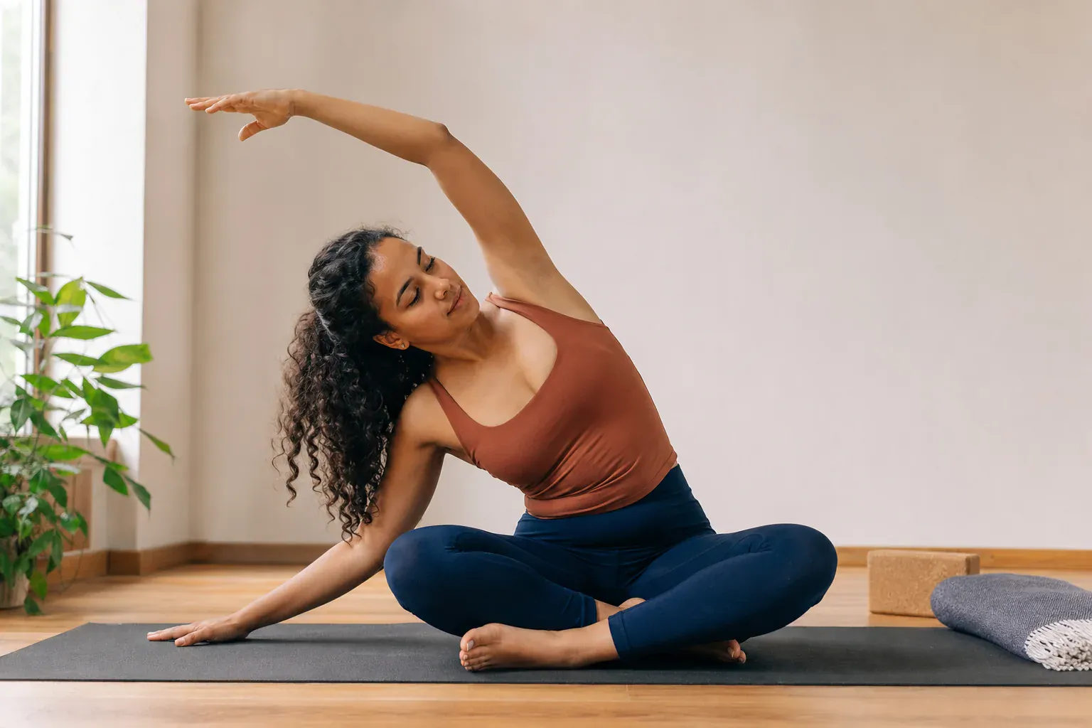 Femme pratiquant un étirement latéral de yoga sur un tapis dans une pièce lumineuse.